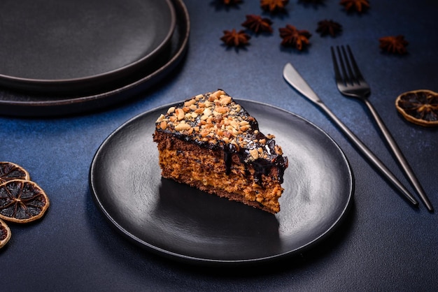 Een stuk verse heerlijke cake met noten en chocolade op een zwarte plaat tegen een donkerblauwe achtergrond