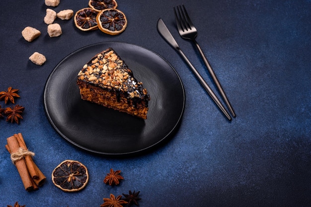 Een stuk verse heerlijke cake met noten en chocolade op een zwarte plaat tegen een donkerblauwe achtergrond