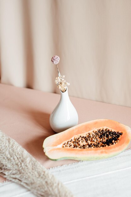 Een stuk verse papaya erop in tweeën gesneden op een bord naast een vaas met eenvoudige bloemen Minimalisme achtergrond natuurlijk concept