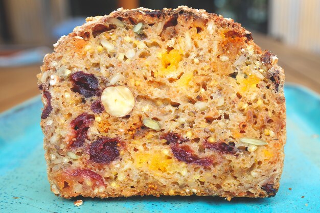 Een stukje brood met gedroogde vruchten op blauw bord, gedroogde abrikozen, rozijnen, pruimen en hazelnoten, bovenaanzicht.