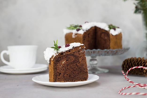 Een stukje kersttaart op bord op grijze tafel met kopje thee en kersttaart op de glazen standaard