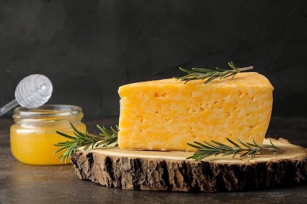 Een stukje smakelijke gemarmerde kaas op een houten standaard met rozemarijn en honing op een donkere achtergrond.