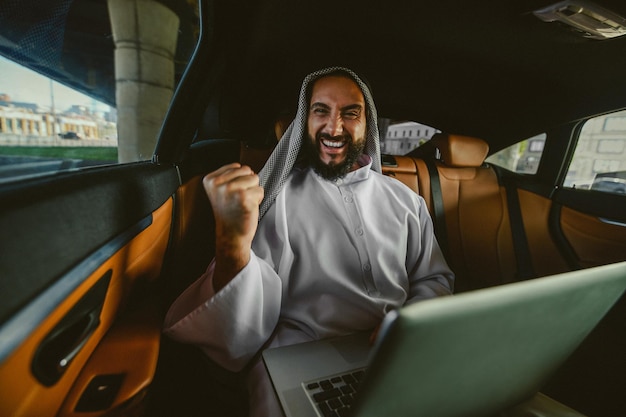 Een suadi-zakenman die op een laptop in een auto werkt