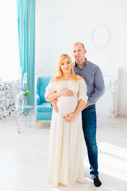 Een succesvolle echtgenoot in een lichte kamer omhelst zijn vrouw die op het kind wacht