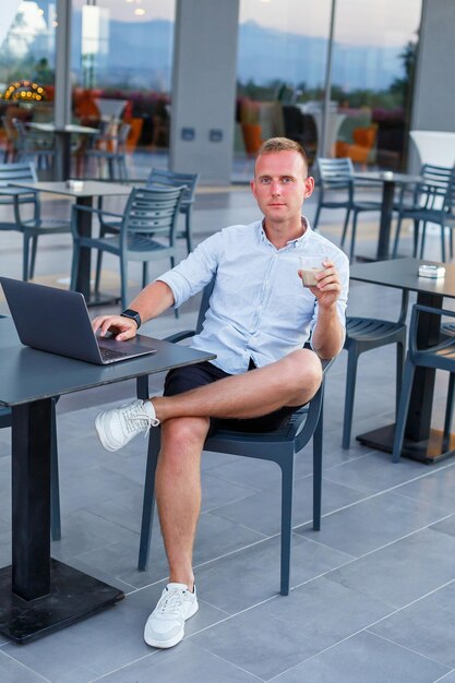 Een succesvolle jonge executive werkt vanaf een laptopbureau op een hotelterras en vindt tijd om werknemers op afstand te beheren terwijl hij op vakantie is in een exotisch resort Man in korte broek en overhemd