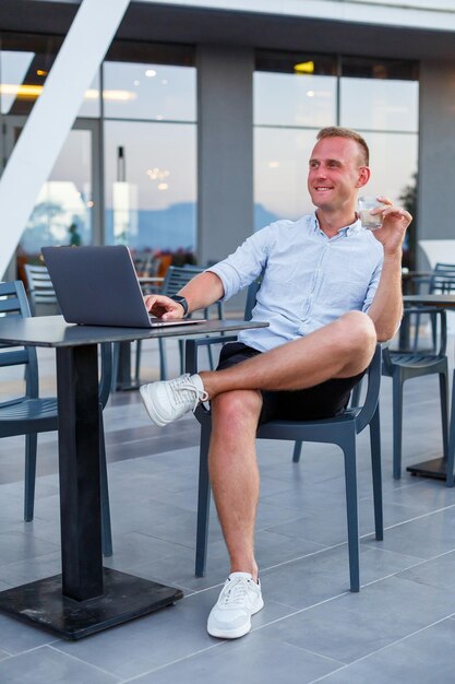 Een succesvolle jonge executive werkt vanaf een laptopbureau op een hotelterras en vindt tijd om werknemers op afstand te beheren terwijl hij op vakantie is in een exotisch resort Man in korte broek en overhemd