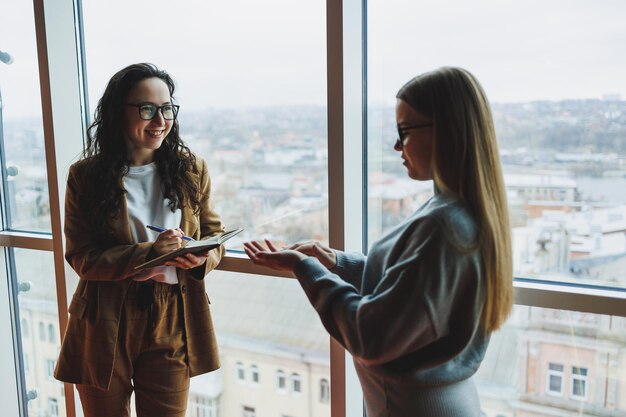 Een succesvolle vrouw met een bril werkt op kantoor op de achtergrond van collega's Moderne werkdag op kantoor Zakenvrouw maakt aantekeningen in een notitieblok