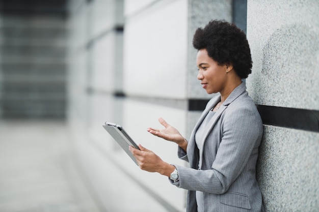 Een succesvolle zwarte zakenvrouw die videogesprek voert op een digitale tablet tijdens een korte pauze voor een bedrijfsgebouw.