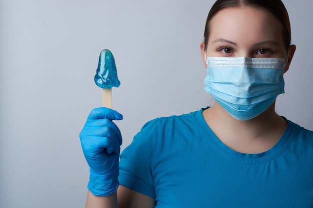 Een suikerende meester in blauwe handschoenen en een medisch masker houdt een stokje blauwe suikerwas vast. ontharing en schoonheidsconcept.