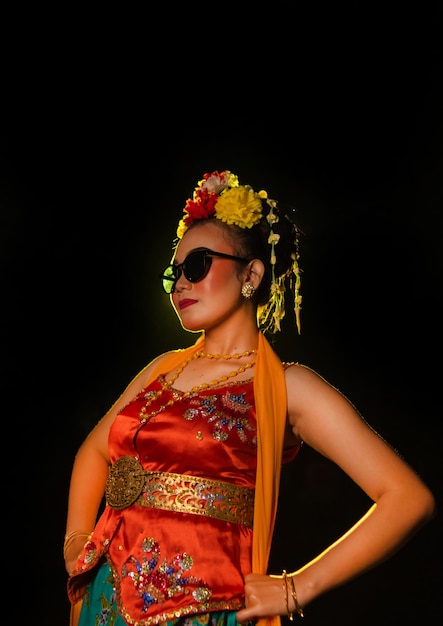 Foto een sundanese danseres poseert voor een schijnend licht terwijl ze een oranje kostuum met zonnebril draagt