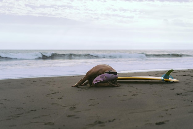 Een surfer loopt met een plank op een zandstrand. Knappe jonge man op het strand. watersport. Gezonde actieve levensstijl. surfen. Zomervakantie. Extreme sporten.