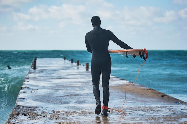 Een surfer met een plank loopt langs de pier om in de oceaan te springen