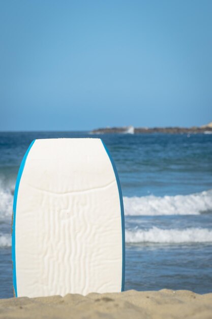 Een surfplank staat op het strand voor de oceaan.