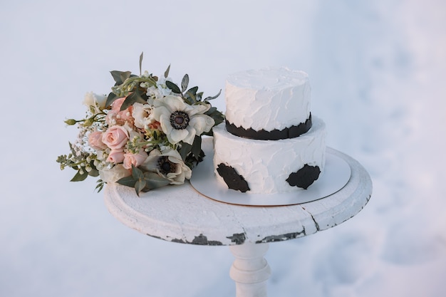 Foto een taart in zwart-wit design, staande op een standaard in een winterbos in de sneeuw.