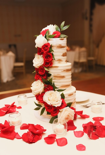 Een taart met drie lagen met rode rozen en witte bloemen