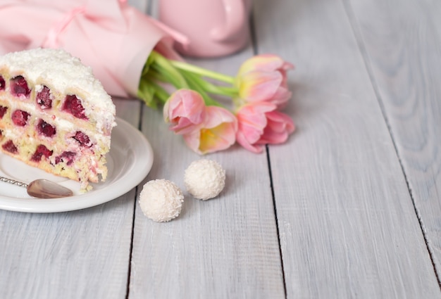 Een taart met kersen en roze tulpen op een witte houten tafel