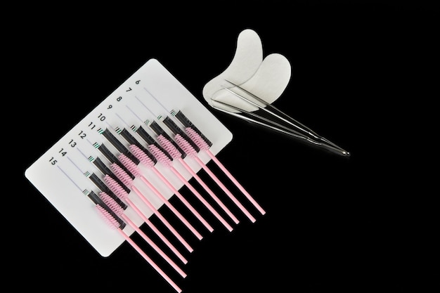 Een tablet met valse wimpers, wimperborstels en patches op een zwarte achtergrond Cosmetische accessoires voor wimperextensies