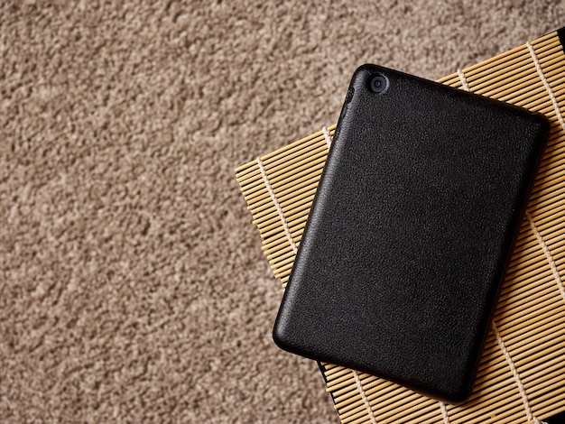 Een tabletcomputer ligt aan de rand van de tafel tegen de achtergrond van de tapijtlaag