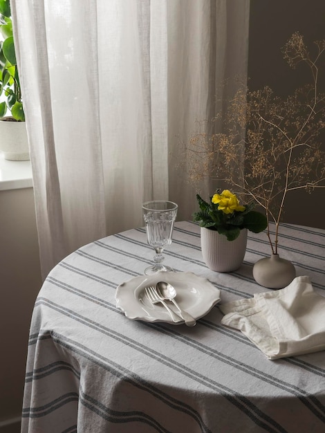 Een tafel voor de lunch een bord bestek glazen op een ronde tafel met een linnen tafellaken bloemen in een pot in de woonkamer