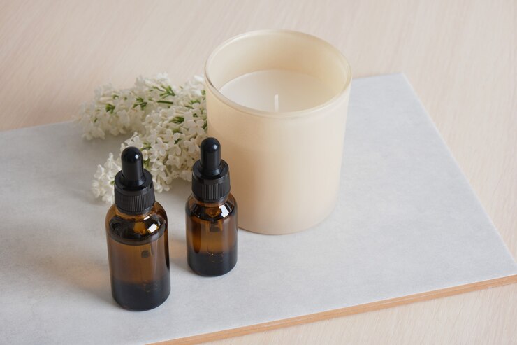 Een tak van witte lila, aromakaars in een glas en bruine flessen met aromaolie in een keramische kom op beige achtergrondkopieerruimte