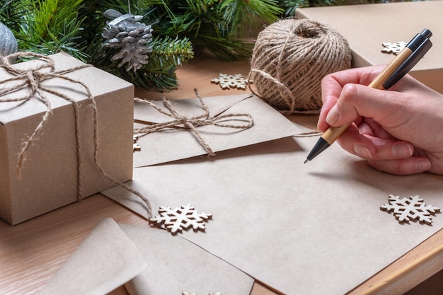 Een takenlijst schrijven, wensenlijst voor nieuwjaarskerst - een hand die met een pen schrijft op leeg gerecycled papier op een tafel met kerstversieringen. Doelen plannen. Geen afval kerstconcept.