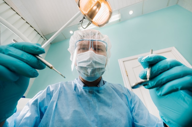 Een tandarts met een beschermend masker zit in de buurt en houdt instrumenten in zijn handen