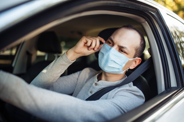 Een taxichauffeur rijdt in een auto en past het medische masker aan tijdens de uitbraak van het coronavirus.