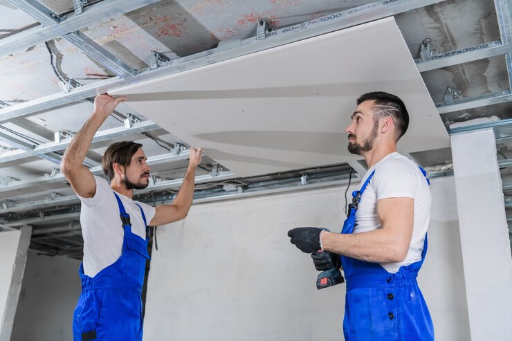 Een team bouwers repareert het plafond in een appartement. Ze dragen blauwe werkkleding