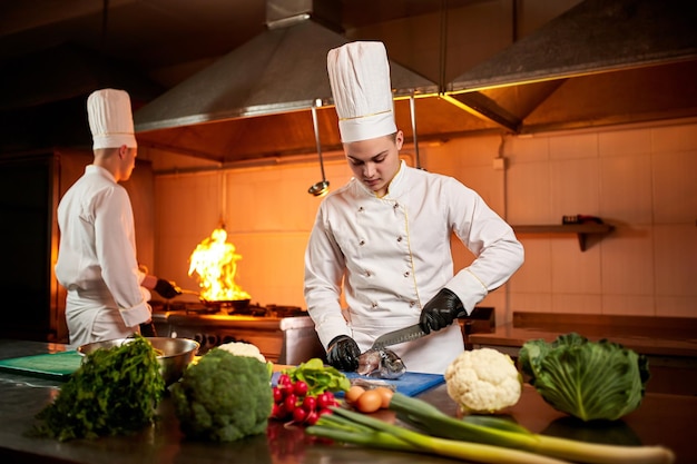 Een team van professionele koks kookt maaltijden met koekenpan en vuur in de keuken van restaurant Chef-kok bereidt schotel met verschillende voedselingrediënten, groenten, vlees en vis