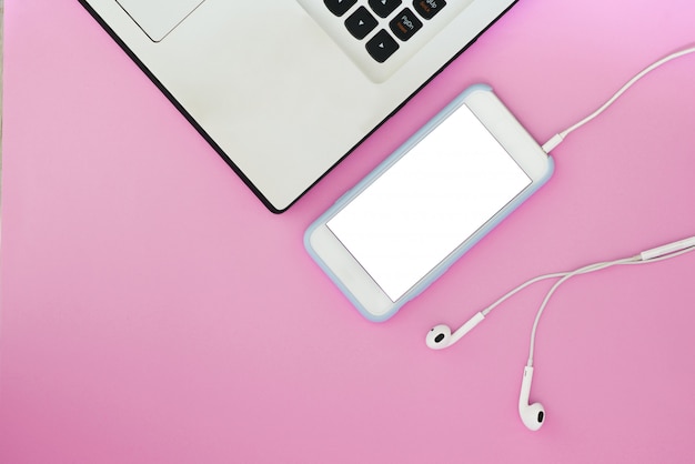 Een telefoon met een wit scherm, een laptop en een koptelefoon op een roze achtergrond en met een plek voor tekst.
