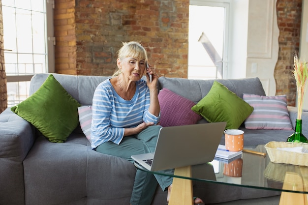 Een telefoontje plegen. Senior vrouw die thuis studeert, online cursussen krijgt, zelfontwikkeling. Blanke vrouw die moderne apparaten gebruikt om plezier te hebben, te leren, tijd door te brengen voor een nieuwe baan of hobby.