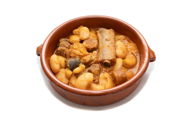 Een terracotta bord met Asturische fabada een typisch Spaanse bonenstoofpot op een witte achtergrond