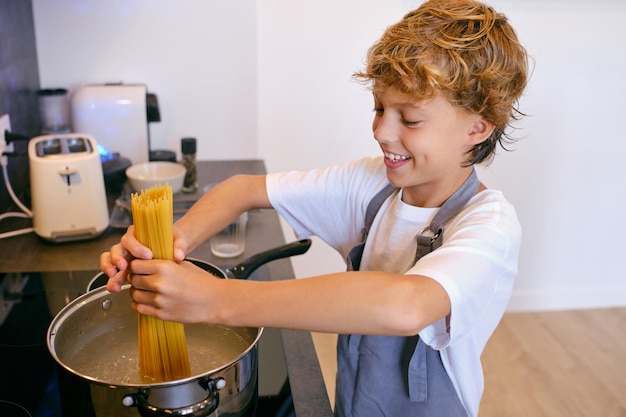 Een tevreden kind zet ongekookte pasta in een pan met kokend water op het kookplaatje in de keuken van het huis