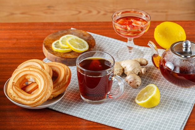 Een theepot sterke thee en een kopje op tafel naast gembercitroen, donuts met room.