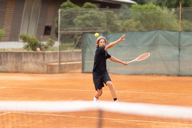 Een tiener in een zwart T-shirt speelt tennis op het veld.