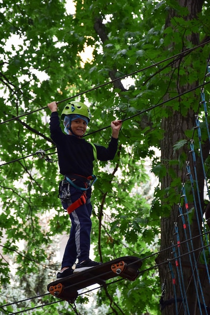 Een tiener met een veiligheidshelm klimt op een hangende ladder in een touwpretpark