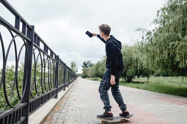 Een tiener met krullend haar van Europees uiterlijk in een zwarte hoodie die op een skateboard in een steegje staat...