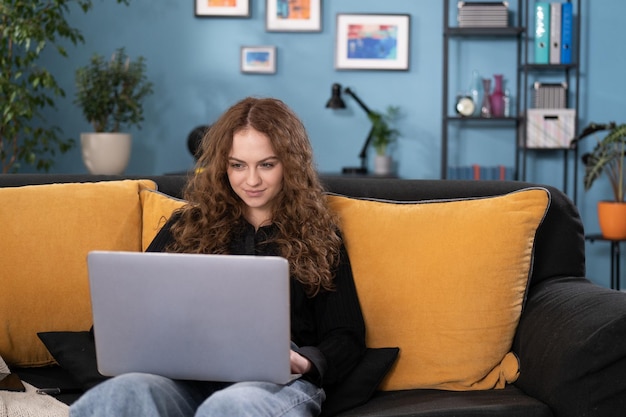 Een tiener ontspant op een bank in de woonkamer thuis, het meisje gebruikt een laptop