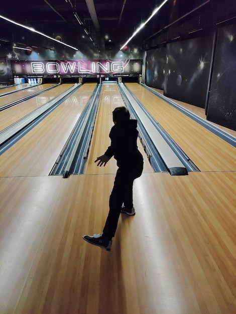 Een tienerjongen speelt bowlen en gooit de bal in de kegels Achteraanzicht