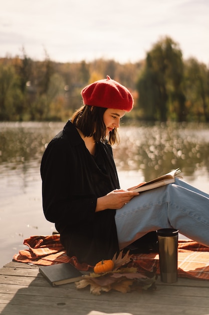 Een tienermeisje in een rode baret leesboek over houten ponton herfstseizoen