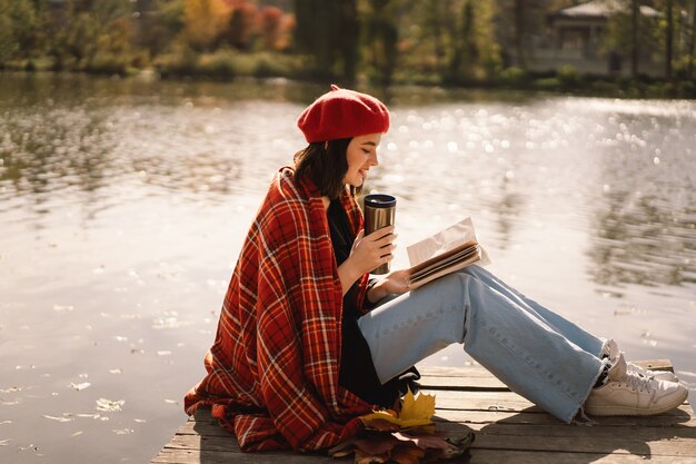 Een tienermeisje in een rode baret leesboek over houten ponton herfstseizoen