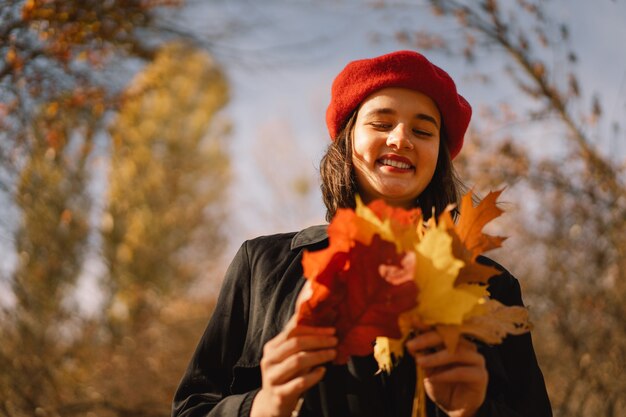 Een tienermeisje in een rode baret met een boeket herfstbladeren in haar handen loopt door het bos