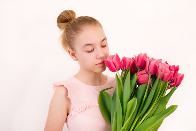 Een tienermeisje in een roze t-shirt met een enorm boeket verse tulpen tegen een witte achtergrond.