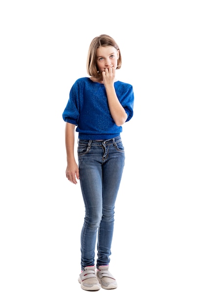 Een tienermeisje in jeans en een blauw sweatshirt bijt op haar nagels. Volledige hoogte. . Verticaal.