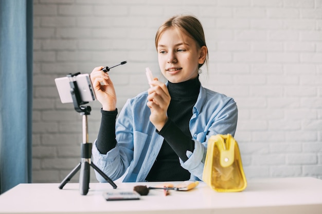 Foto een tienermeisje maakt make-up en neemt video's op voor haar blog op een smartphone op een statief thuis