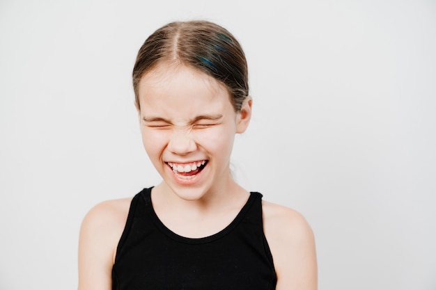 Foto een tienermeisje met verzamelde haren in een zwart t-shirt staat op een witte ondergrond en lacht met tanden.