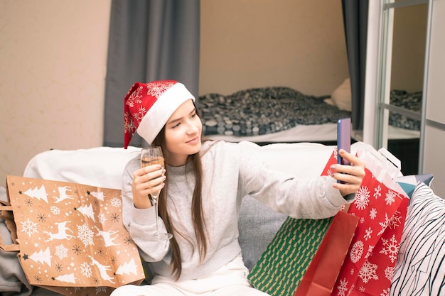 Foto een tienermeisje praat online met haar familie via een videolink, laat cadeaus zien en wenst hen een vrolijk kerstfeest en een gelukkig nieuwjaar met een glas champagne