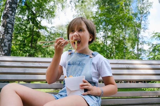 Een tienermeisje tijdens een wandeling op een zomerdag in het park luncht met noedelswok