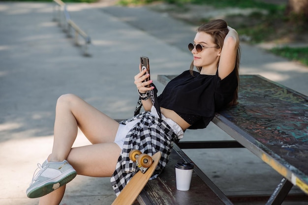 Een tienerschaatsermeisje is aan het chillen op de bank met een skateboard in het skaterspark