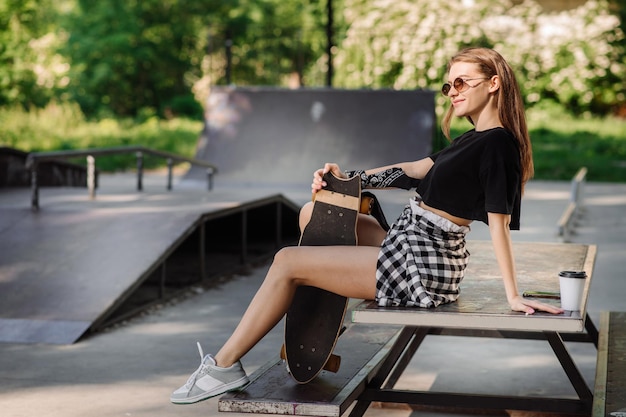 Een tienerschaatsermeisje is aan het chillen op de bank met een skateboard in het skaterspark